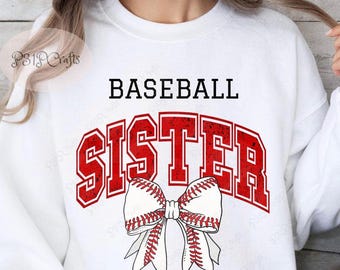 May include: A white crewneck sweatshirt featuring the black text BASEBALL above the red distressed text SISTER. Below the word SISTER is a graphic of a white hair bow with red baseball-style stitching patterns across the fabric.