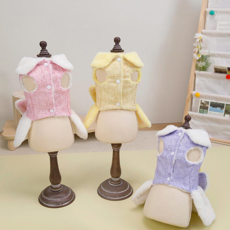 K&ouml;nnte beinhalten: Drei Hundejacken in Rosa, Gelb und Lavendel, pr&auml;sentiert auf Schaufensterpuppen. Jede Jacke hat eine tweedartige Textur, einen wei&szlig;en Fellbesatz und Knopfverschl&uuml;sse. Die Jacken sind mit &Ouml;ffnungen f&uuml;r die Beine und den Kopf des Hundes versehen.