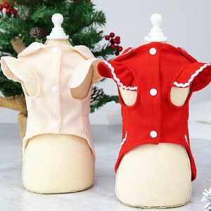 May include: Two pet dresses, one red and one cream, with white trim and buttons. The dresses are on mannequins and have a ruffled neckline.