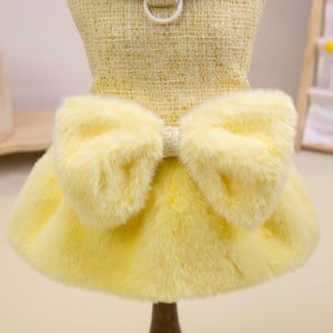 K&ouml;nnte beinhalten: Gelbes Hundekleid mit strukturiertem Oberteil und flauschigem Rock. Das Kleid hat eine gro&szlig;e Schleife aus weichem, gelbem Kunstfell. Entworfen f&uuml;r kleine Hunde.