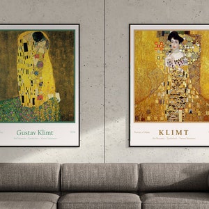May include: Two framed posters of paintings by Gustav Klimt. The left poster features "The Kiss" with two figures in a golden embrace. The right poster features "Portrait of Adele Bloch-Bauer I" with a woman in a gold gown. Both posters have a white background with black text.