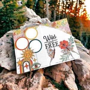 May include: A planner with a floral design on the cover. The planner has a page with a sun, rainbow, and eye design. The other page has the text "Wild and FREE" with butterflies and flowers.