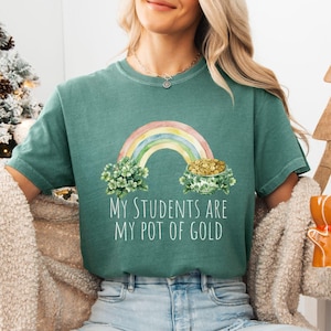 May include: A teal green t-shirt with a rainbow and pot of gold graphic. The text on the shirt reads "My students are my pot of gold."