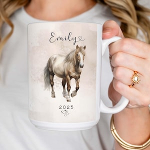 May include: White ceramic mug with a watercolor illustration of a light brown horse. The mug has the name "Emily" and the year "2025" printed on it.