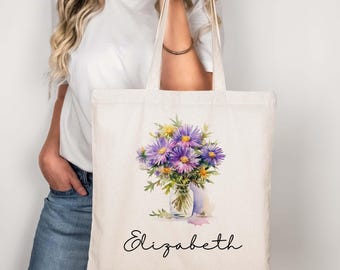 Puede incluir: Una bolsa de lona blanca con una ilustración de acuarela de un ramo de flores moradas en un jarrón de vidrio. El nombre "Elizabeth" está impreso en cursiva negra debajo de las flores.