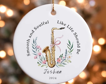 May include: White ceramic ornament with a gold-colored saxophone, surrounded by floral accents and the text "Smooth and Soulful, Like Life Should Be." Includes the name "Joshua" and the year "2024".