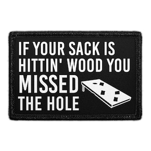 May include: Black rectangular patch with white text that reads "IF YOUR SACK IS HITTIN' WOOD YOU MISSED THE HOLE." A white illustration of a cornhole board is on the right side.