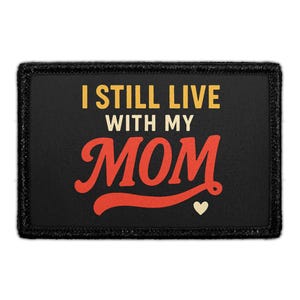 May include: Black rectangular patch with the text "I STILL LIVE WITH MY MOM" in yellow and white. The word "MOM" is in red script with a small white heart below it. The patch has a black border.