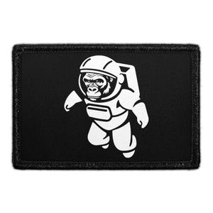 May include: A rectangular black patch featuring a white embroidered graphic of a gorilla wearing an astronaut helmet and space suit. The design shows the gorilla from the chest up, centered on the black fabric background with a stitched border.