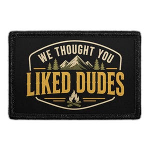 May include: Black rectangular patch with the text "WE THOUGHT YOU LIKED DUDES" in white and yellow. The patch features a mountain range, pine trees, and a campfire graphic. The patch has a black border.