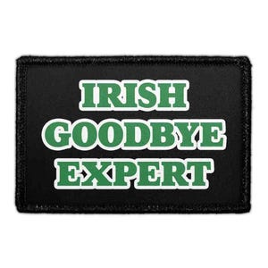 May include: A rectangular black patch with a stitched border featuring the text IRISH GOODBYE EXPERT in bold green capital letters with a white outline. The lettering is arranged in three stacked lines centered on the black fabric background.