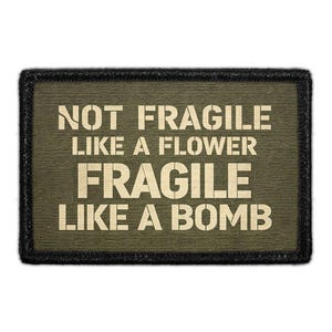May include: Olive green rectangular patch with the text "NOT FRAGILE LIKE A FLOWER FRAGILE LIKE A BOMB" in a stencil font. The patch has a black border.