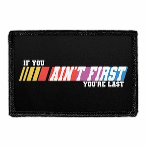 May include: A rectangular black patch with a stitched border. The text IF YOU AIN'T FIRST YOU'RE LAST is printed in white. To the left of the text are three vertical stripes in yellow, orange, and red, followed by a blue stripe behind the word FIRST.