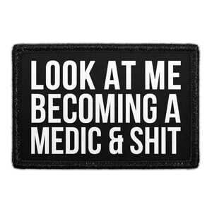 May include: A rectangular black patch with a stitched border featuring the white text "LOOK AT ME BECOMING A MEDIC & SHIT" in a bold, sans-serif font. The design is centered on the black fabric background, creating a high-contrast, legible appearance.