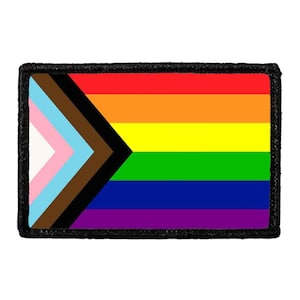 May include: A rectangular embroidered patch featuring the Progress Pride flag design. The flag includes horizontal stripes of red, orange, yellow, green, blue, and violet, with a chevron on the left side containing white, pink, light blue, brown, and black.