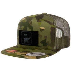 May include: A camouflage print snapback hat with a black patch featuring a white design. The hat has a curved brim and a mesh back. The brim has a small red and white tag. The hat is a snapback style.
