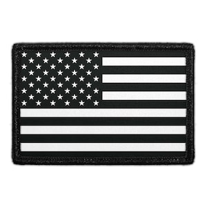 May include: A rectangular patch featuring a black and white version of the American flag. The design includes a black canton with white stars and alternating black and white horizontal stripes, all enclosed within a thick black stitched border.