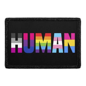 May include: A rectangular black patch featuring the word HUMAN in large capital letters. Each letter is filled with a different pride flag pattern, including asexual, bisexual, rainbow, transgender, and pansexual color schemes on a black background.
