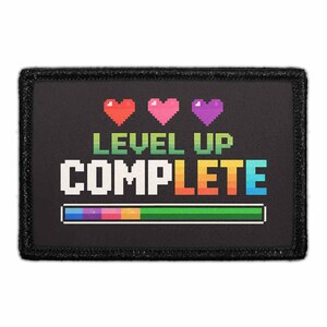 May include: A rectangular black patch featuring pixel art graphics. At the top are three pixelated hearts in red, pink, and purple. Below, the text reads LEVEL UP COMPLETE in a multi-colored pixel font. A loading bar at the bottom shows a gradient.