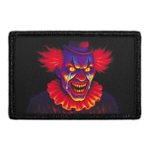 May include: A rectangular patch featuring a colorful, menacing clown face. The clown has red hair, a ruffled collar, and a hat. The clown's face is painted in shades of blue, purple, and yellow, with glowing yellow eyes and a sinister grin.