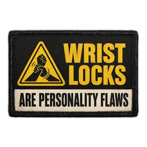 May include: A rectangular black patch with a yellow warning triangle containing a graphic of two hands performing a wrist lock. The text WRIST LOCKS appears in yellow, and the text ARE PERSONALITY FLAWS appears in black on a cream background.