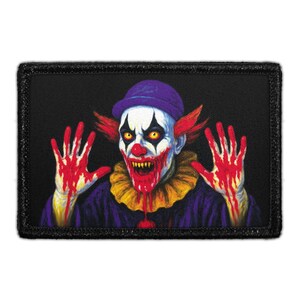 May include: A rectangular embroidered patch featuring a clown with a purple hat, yellow eyes, and sharp teeth. The clown has red hair, a yellow ruffled collar, and a purple shirt. Both hands are raised, covered in bright red blood-like stains.