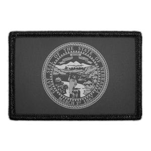 May include: A rectangular black patch featuring the Great Seal of the State of Nebraska in a light gray monochromatic design. The seal depicts a blacksmith, mountains, and a river with the text Great Seal of the State of Nebraska March 1st 1867.