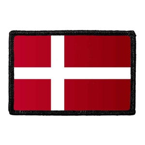May include: A rectangular embroidered patch featuring the national flag of Denmark, which consists of a red field with a white Nordic cross that extends to the edges of the emblem. The patch is finished with a thick, black stitched border.