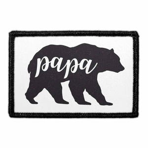 May include: A rectangular iron-on patch with a white background and a thick black stitched border. The center features a solid black silhouette of a walking bear with the word "papa" written in white cursive script across its body.