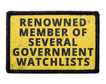 Könnte beinhalten: Ein rechteckiger Aufnäher mit gelbem Hintergrund und schwarzem Rand. Der Text RENOWNED MEMBER OF SEVERAL GOVERNMENT WATCHLISTS ist in schwarzen, abgenutzten Großbuchstaben in der Mitte des Aufnähers aufgedruckt, was ihm ein gealtertes Aussehen verleiht.