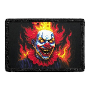May include: A rectangular patch featuring a menacing clown with fiery red hair and a sinister grin. The clown's face is painted with blue, white, and red details, and it is surrounded by flames. The patch has a black border.