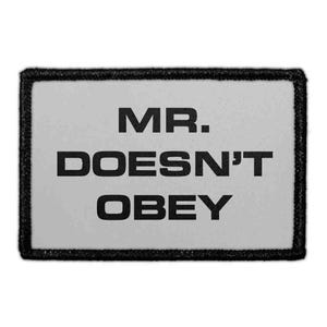 May include: A rectangular patch with a light gray background and a thick black border. The text MR. DOESN'T OBEY is printed in bold, black, sans-serif capital letters across the center of the patch, arranged in three distinct lines.