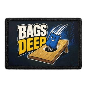 May include: A rectangular morale patch with a black border featuring a cartoon illustration of a blue bean bag with a face winking as it falls into a wooden cornhole board hole. The text BAGS DEEP is printed in large white and yellow letters.
