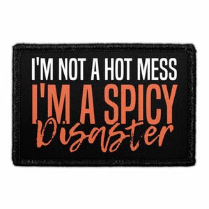 May include: A rectangular black patch with a stitched border featuring the white text I'M NOT A HOT MESS and the orange text I'M A SPICY DISASTER. The word DISASTER is written in a stylized, handwritten script font, while the rest is sans-serif.