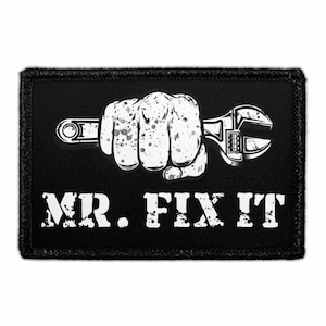 May include: Black patch with a white graphic of a clenched fist holding a wrench. The text "MR. FIX IT" is below the graphic in white, distressed lettering. The patch has a black border.