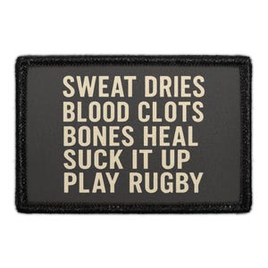 May include: A rectangular black patch with a stitched border featuring the beige text: SWEAT DRIES, BLOOD CLOTS, BONES HEAL, SUCK IT UP, PLAY RUGBY. The design is centered on a dark fabric background with clear, bold, sans-serif capital lettering.