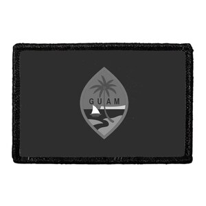 May include: A rectangular patch featuring a dark gray background with a central almond-shaped emblem. The emblem displays a palm tree, a small sailboat, and the text GUAM in black lettering, all rendered in monochromatic shades of gray and black.