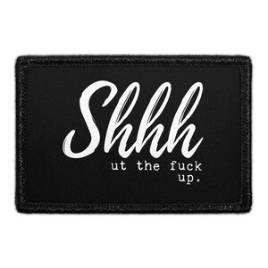 May include: A rectangular black patch with a stitched border featuring the white text Shhhh in a large script font and the smaller white text ut the fuck up. in a typewriter-style font centered on the fabric surface of the rectangular patch.