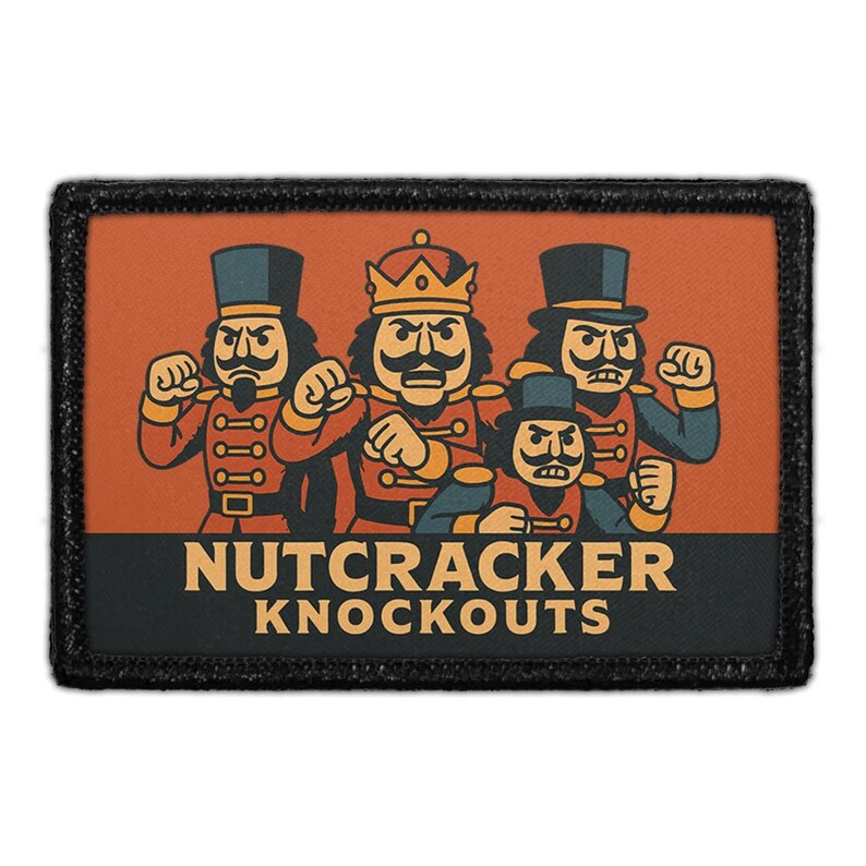 Op de afbeelding: Een rechthoekige patch met een zwarte rand toont een cartoonillustratie van vier notenkrakerfiguren in verschillende poses. De figuren dragen rode, zwarte en gouden uniformen. De tekst "NUTCRACKER KNOCKOUTS" wordt vetgedrukt weergegeven.