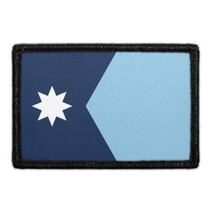 May include: A rectangular patch with a black stitched border. The design features a dark blue section on the left with a white eight-pointed star and a light blue section on the right, separated by a vertical chevron-like dividing line.