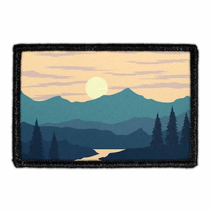 May include: A rectangular embroidered patch featuring a landscape illustration of layered blue mountains, a pale yellow sun, and dark blue pine trees against a light peach sky. The entire scene is framed by a thick, solid black stitched border.