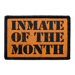 May include: A rectangular patch with a black border and an orange background. The text INMATE OF THE MONTH is printed in a bold, black, distressed serif font across three lines, centered on the orange surface of the rectangular patch.