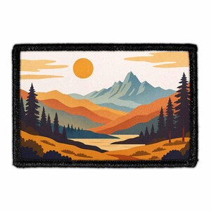 May include: Rectangular patch featuring a landscape scene with mountains, a lake, and trees. The artwork uses warm colors like orange, brown, and yellow, with a bright yellow sun in the sky. The patch has a black border.