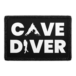 May include: A rectangular black patch with a white embroidered border. The text CAVE DIVER is printed in bold white capital letters. The letter A in CAVE is replaced by a white silhouette of a mountain peak, and the letter I in DIVER is a diver.