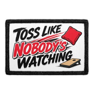 May include: A rectangular patch with a black border featuring the text TOSS LIKE NOBODY'S WATCHING in black and red lettering. The design includes a red bean bag in motion and a wooden cornhole board on a white background.