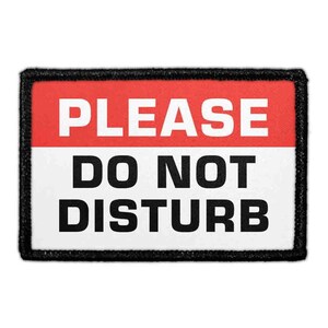 May include: A rectangular patch with a black border and the words "PLEASE DO NOT DISTURB" in bold white letters on a red and white background. The patch is likely for a door or a wall.