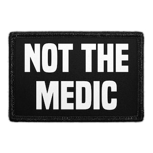 May include: A rectangular black patch with the white text "NOT THE MEDIC". The patch has a black border with a textured appearance. The text is in a bold, sans-serif font.