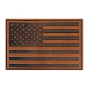 May include: A rectangular leather patch featuring a debossed American flag design. The surface displays a dark brown, textured finish with the stars and stripes pattern pressed into the material, creating a distinct contrast between the raised and recessed areas.