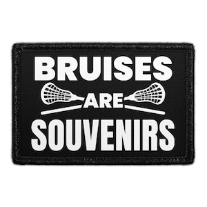 May include: A rectangular black patch with a stitched border featuring the white text BRUISES ARE SOUVENIRS. Between the words ARE and SOUVENIRS, there are two white lacrosse stick graphics crossed horizontally across the center of the patch.