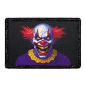 May include: A rectangular patch featuring a menacing clown face. The clown has blue skin, red hair, and a wide, toothy grin. It wears a purple shirt with a yellow ruffled collar, set against a black background.